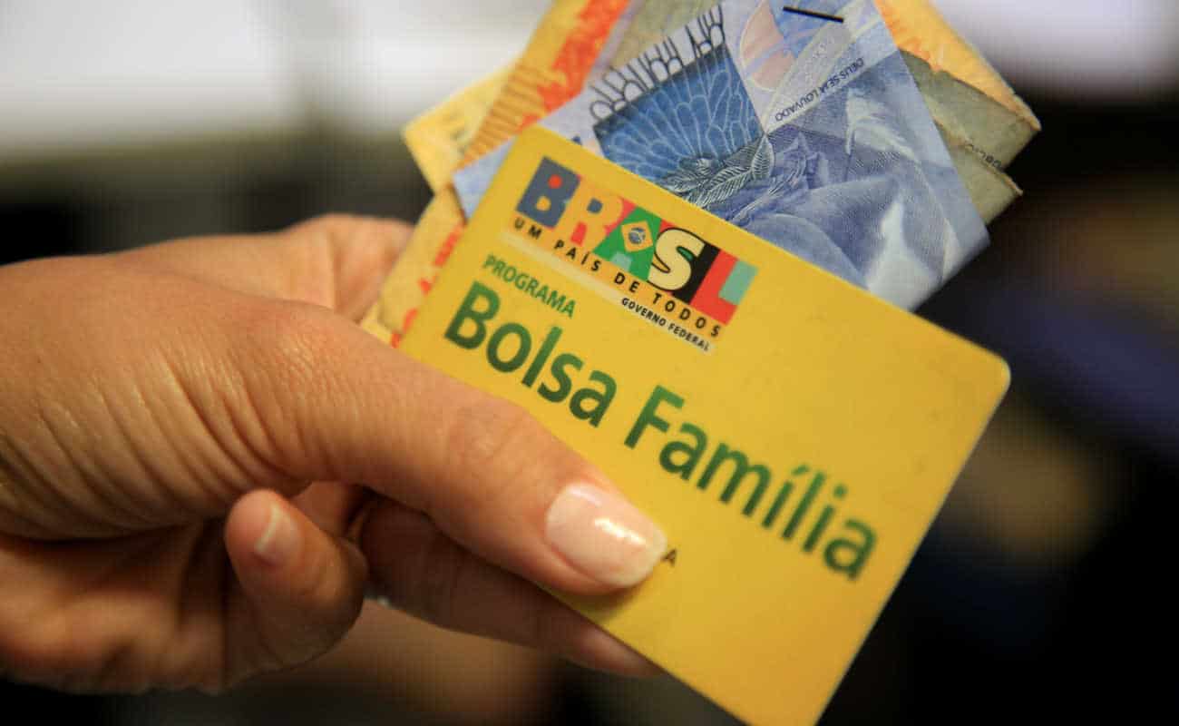 Mulher segurando o cartão do Bolsa Família e algumas notas de dinheiro