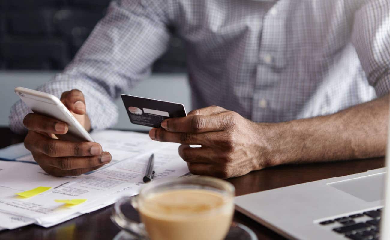 Homem usando um smartphone em uma mão para acessar banco digitale um cartão na outra