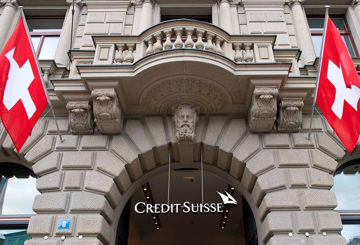 Imagem da fachada do banco Credit Suisse, com duas bandeiras da Suíça