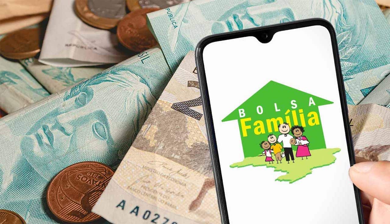 celular com página do Bolsa Família aberta, mostrando desenho de uma família e uma casa verde, ao fundo, notas de dinheiro e moedas