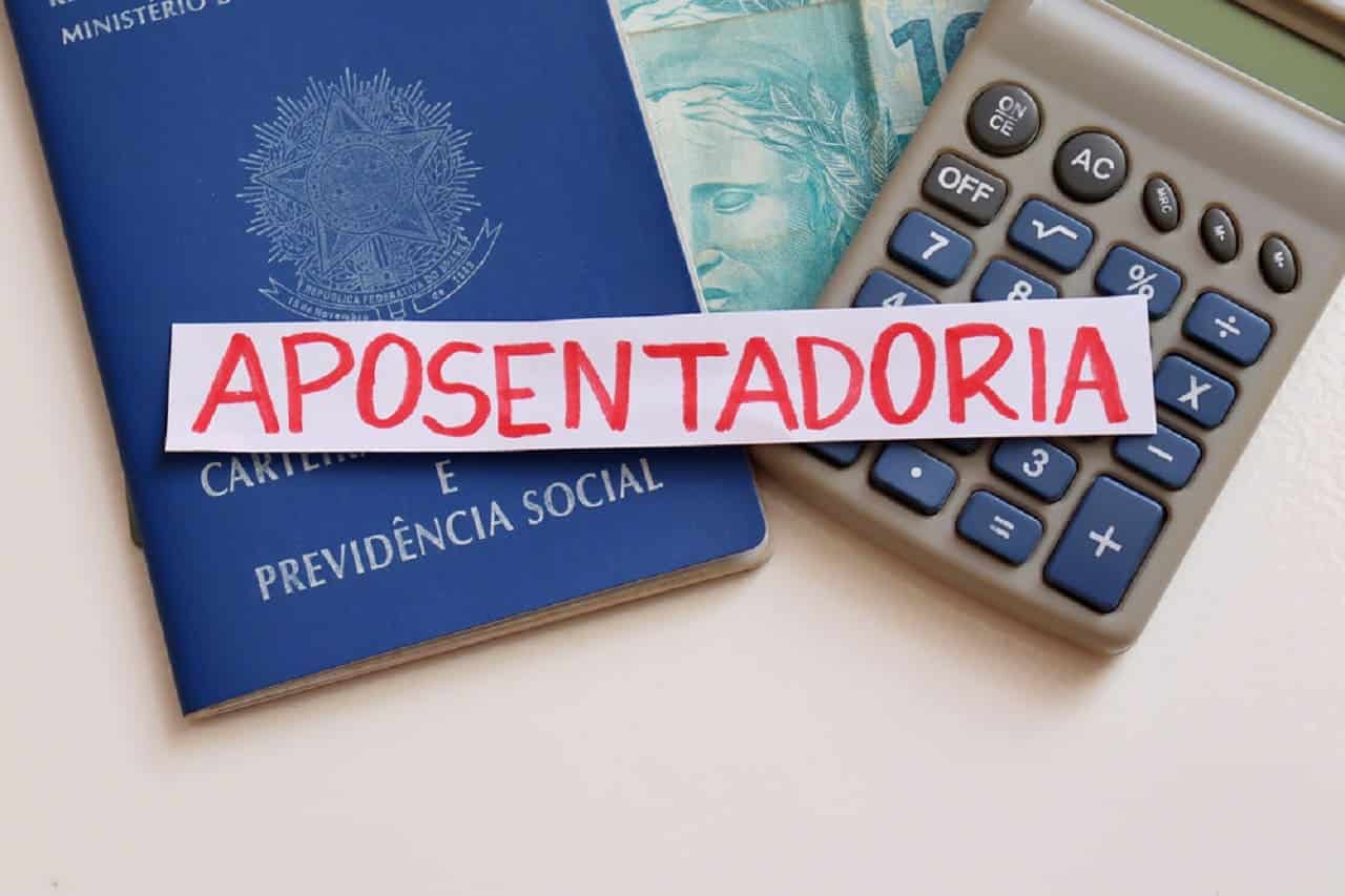 Imagem de uma calculadora, uma nota de R$100, uma carteira de trabalho e um papel escrito "aposentadoria".