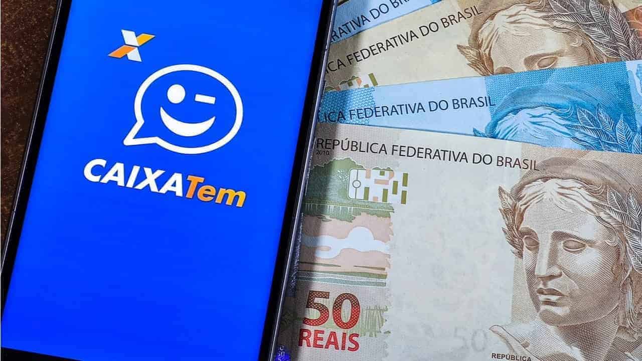 Ao lado de notas de real, celular exibe tela inicial do Caixa Tem