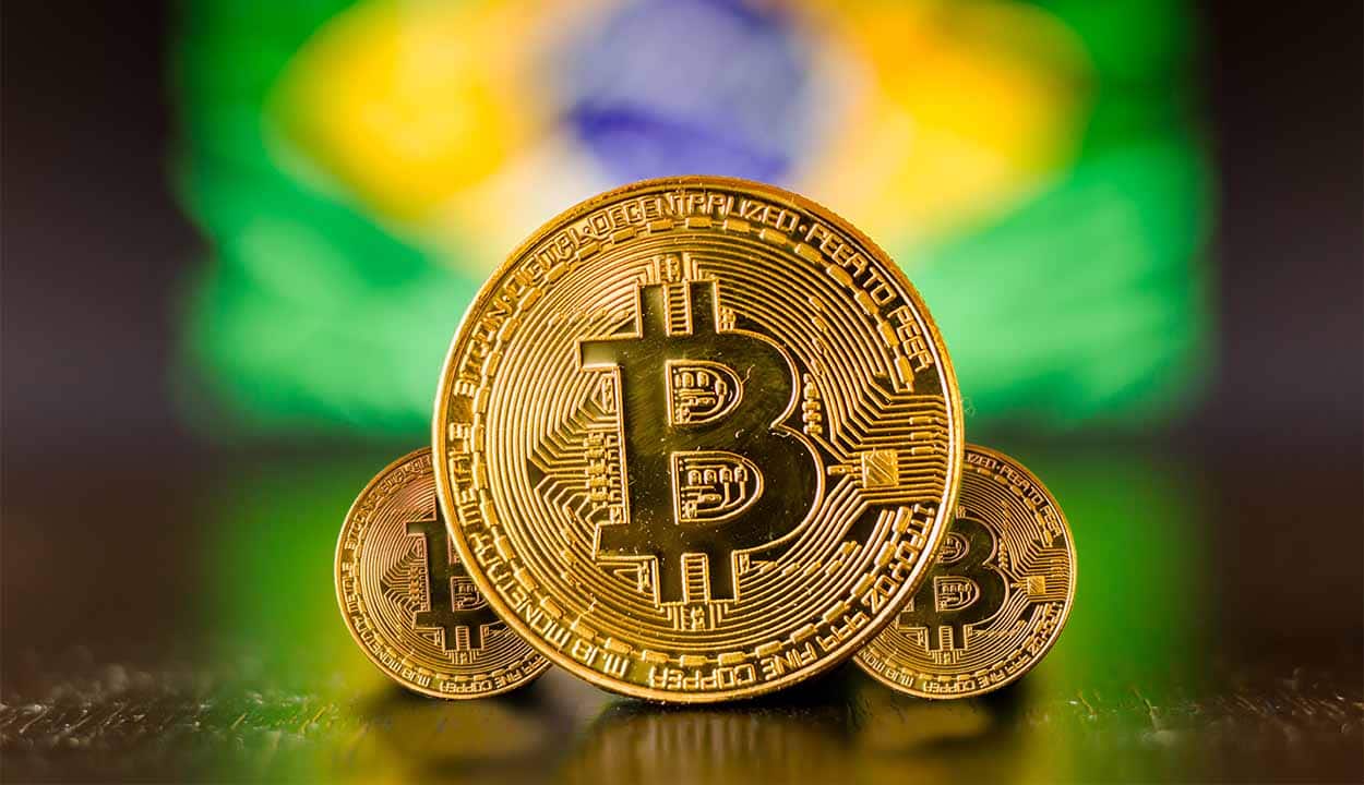 criptomoeda em primeiro plano, ao fundo bandeira do Brasil desfocada.