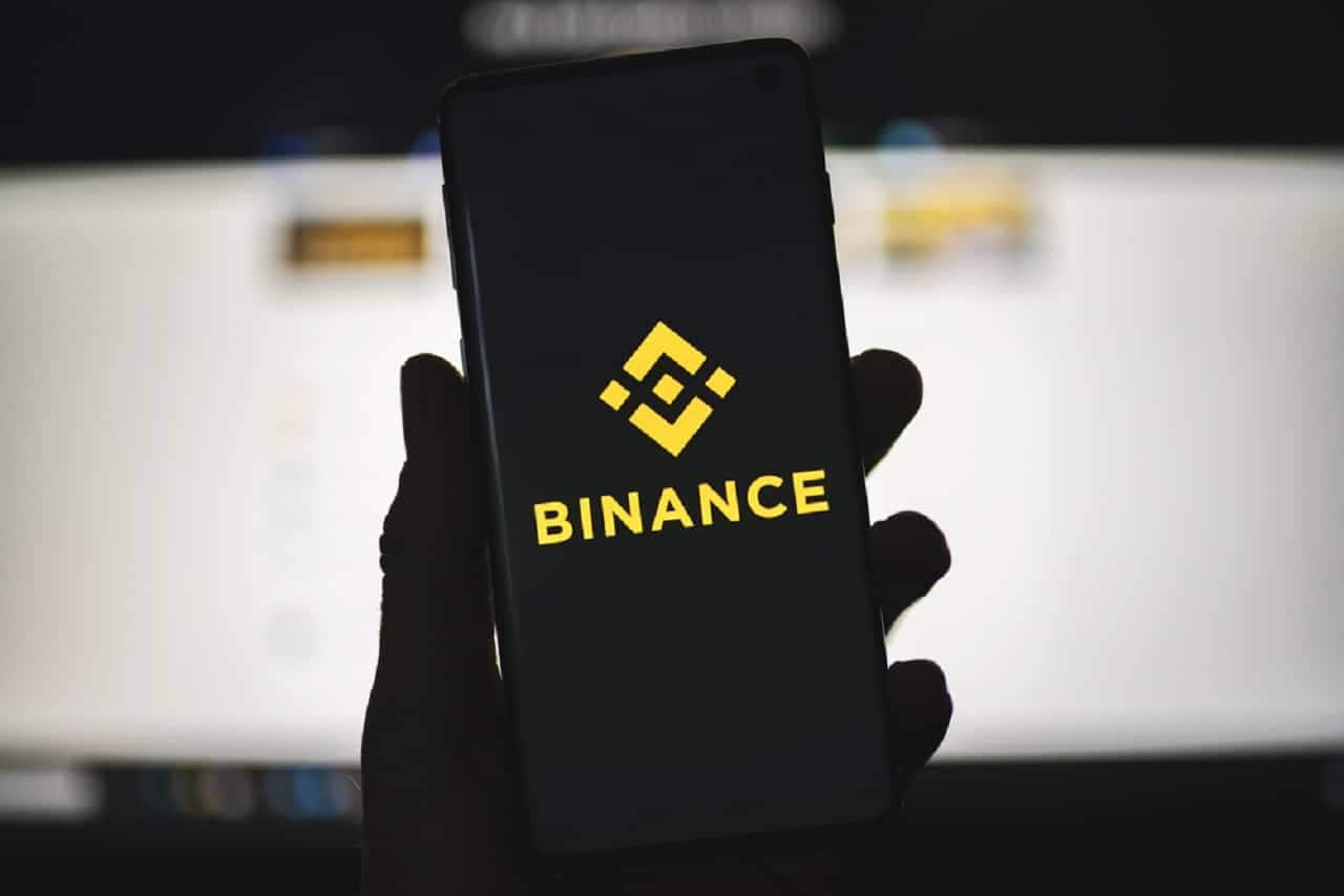 Mão segurando um celular com a tela ligada na logo da corretora Binance
