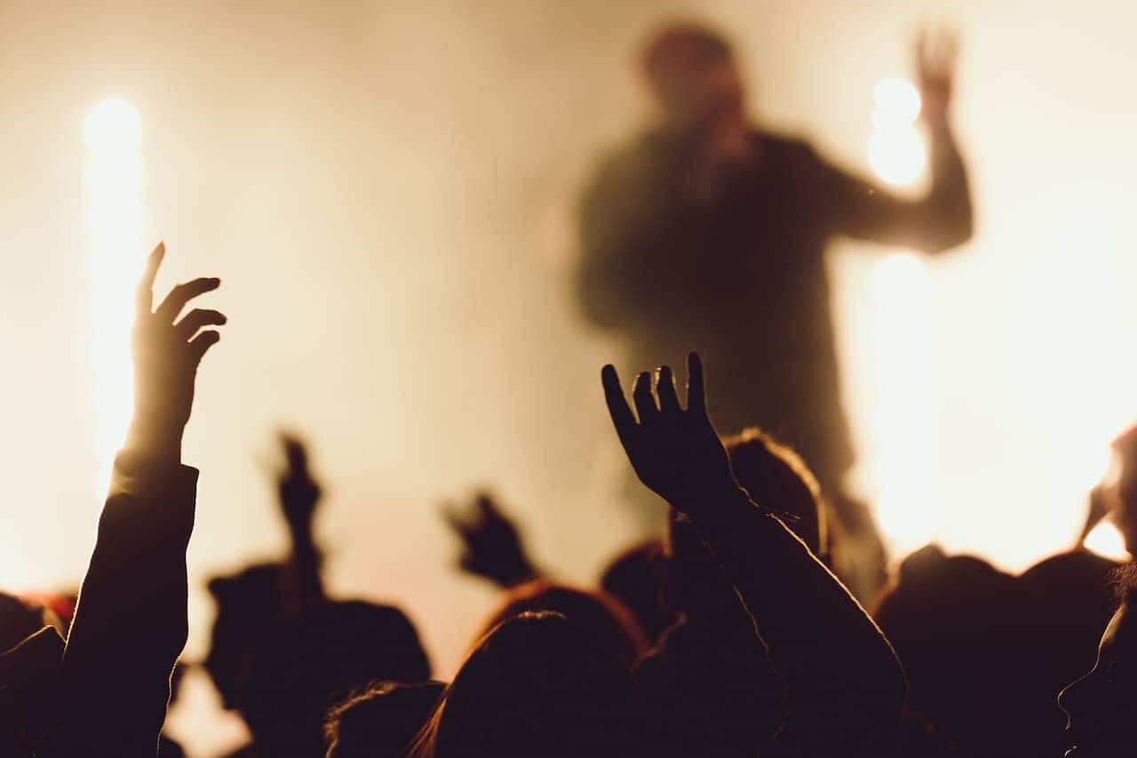 cantor em cima do palco, cercado por luzes, sendo acompanhado pelo público.