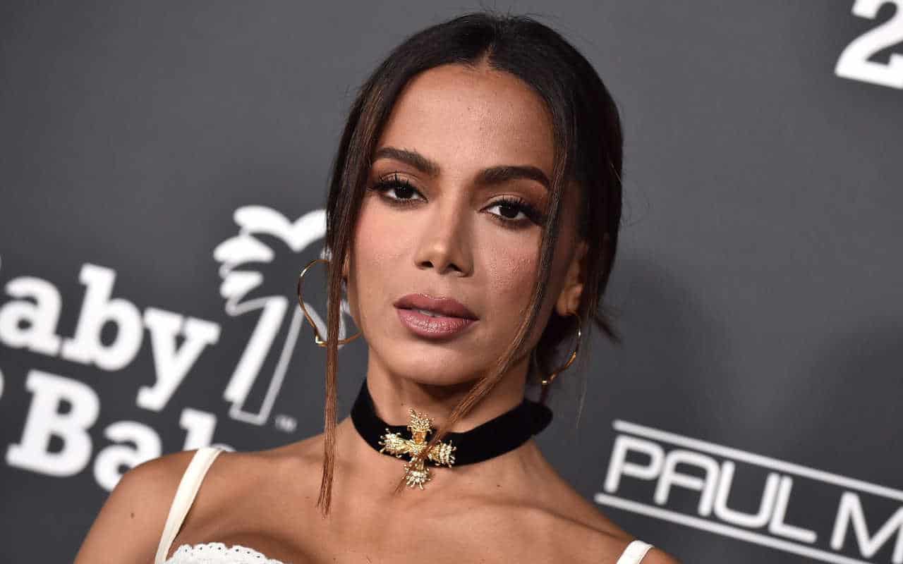 Foto da cantora Anitta no que parece ser a entrada de um evento. A foto pega só seu busto, mas, pelos detalhes do fundo, parece ser um tapete vermelho