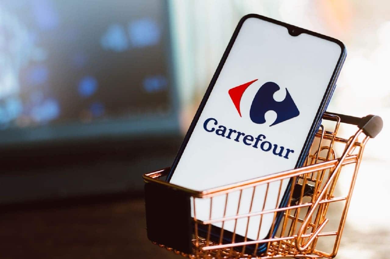 Imagem de um celular com o aplicativo do carrefour aberto. Está dentro de um pequeno carrinho de supermercado.