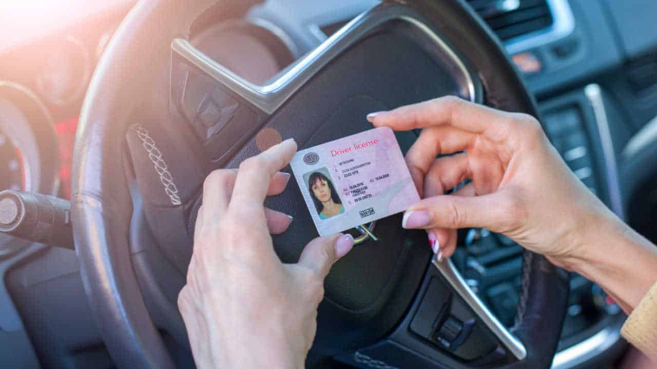 as mãos femininas segurando uma carteira de motorista dos EUA, sobre o volante do carro