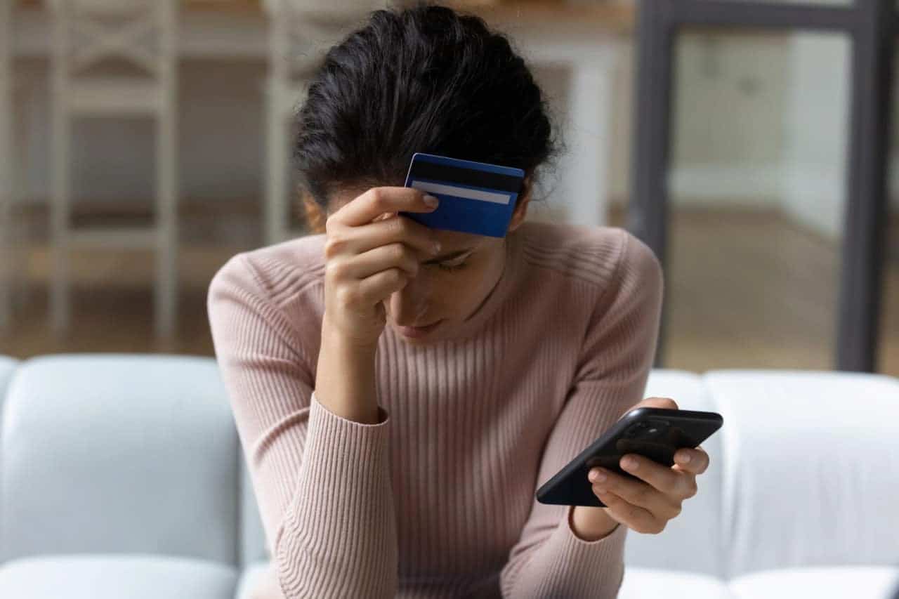 Mulher sentada com celular e cartão na mão