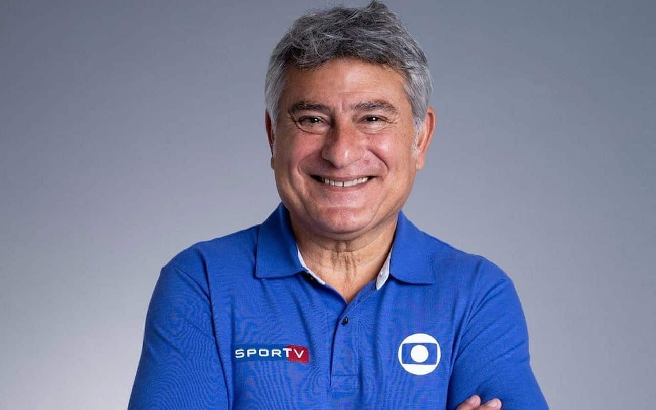 Foto de narrador e apresentador esportivo Cléber Machado, vestido com uma camisa de gola polo azul com logo do SporTV e da Rede Globo