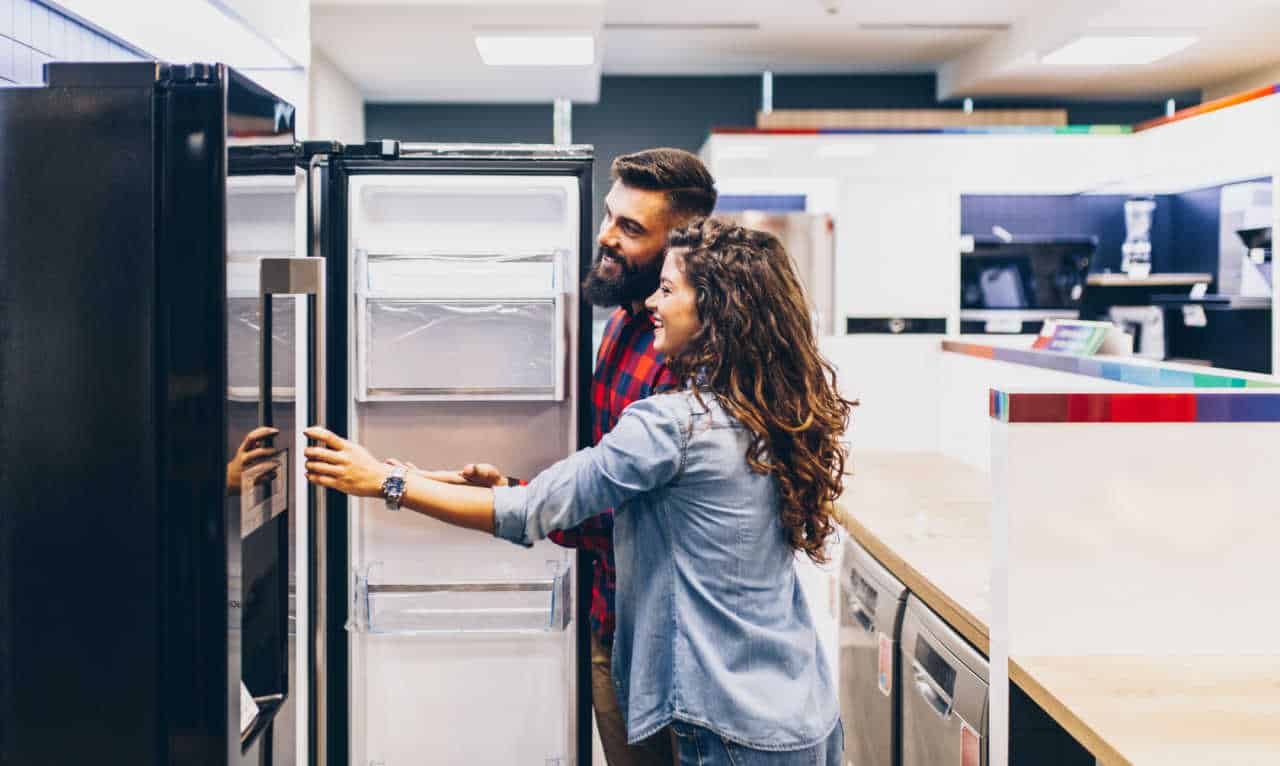 Casal abrindo uma geladeira dentro de uma loja de produtos de casa.