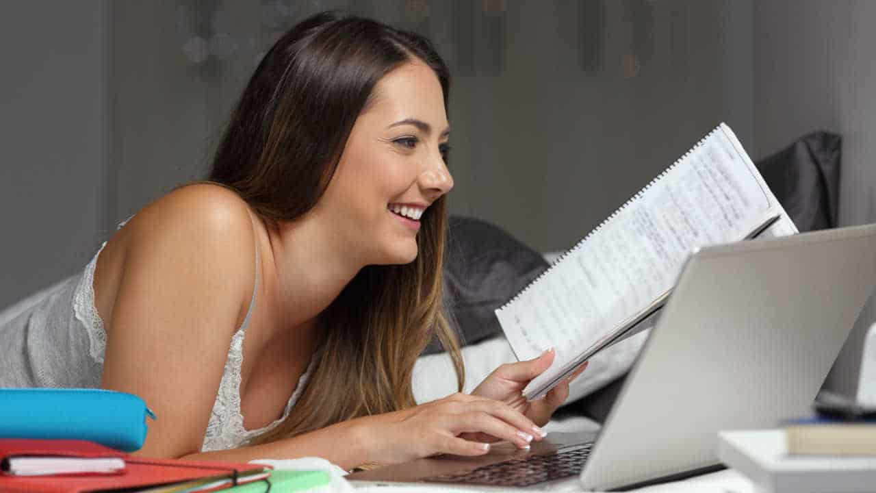 mulher estudando com um notebook e vários cadernos na cama