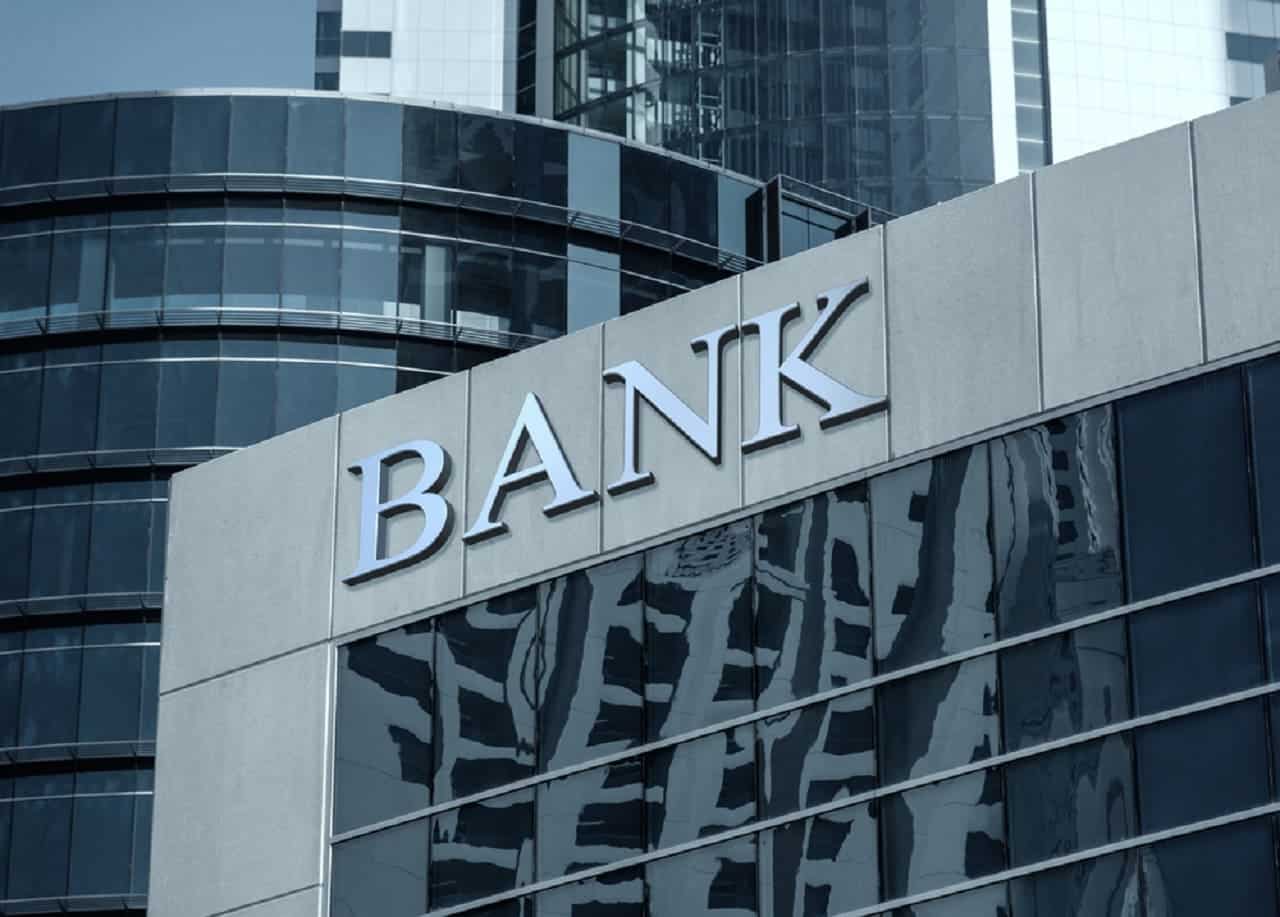 Imagem da fachada de um banco. Ao fundo, prédios.