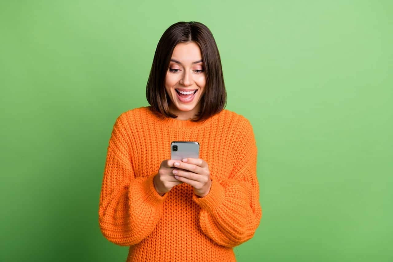 Mulher olhando para um celular enquanto sorri. Fundo verde
