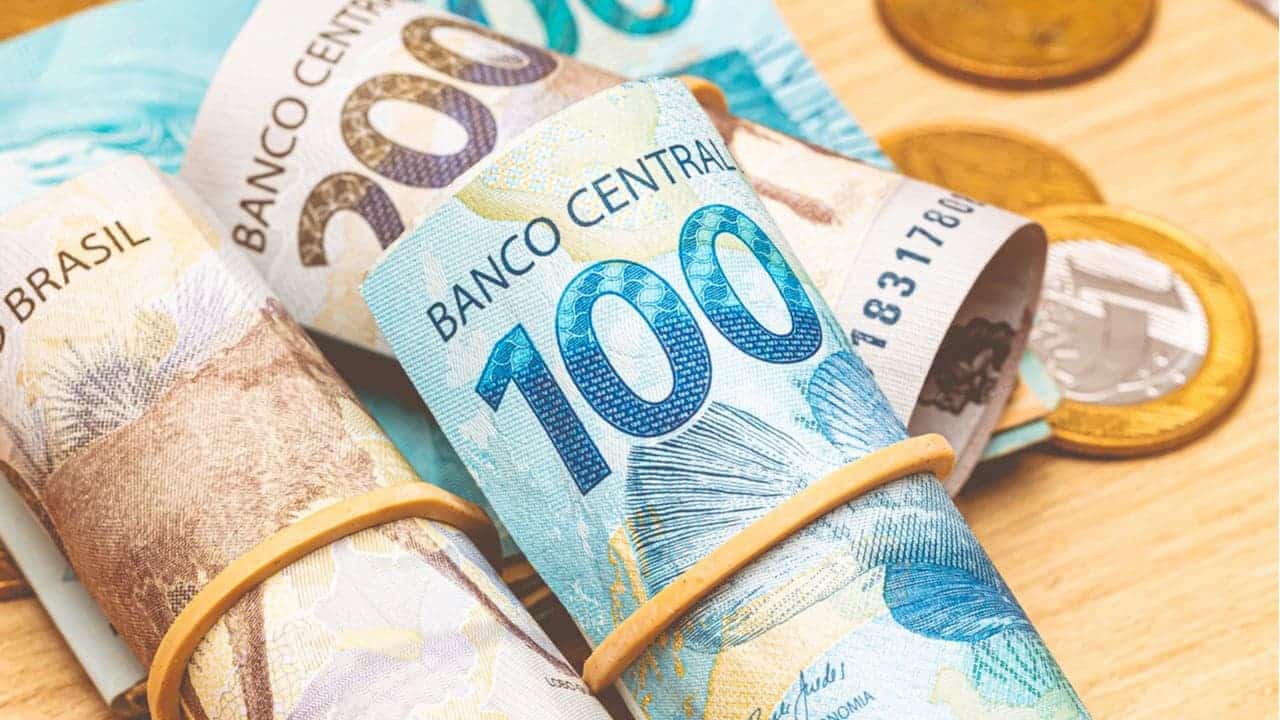 várias notas de real enroladas em elásticos e algumas moedas ao lado