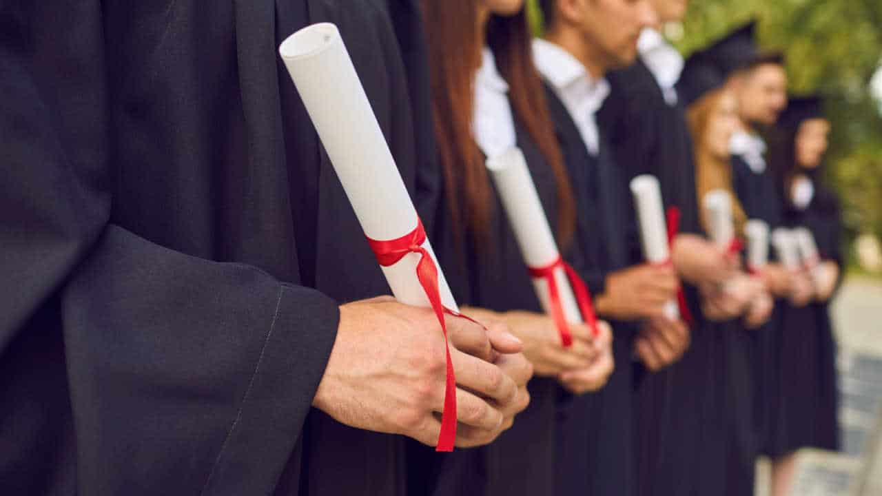 Universitários com beca e diploma na mão