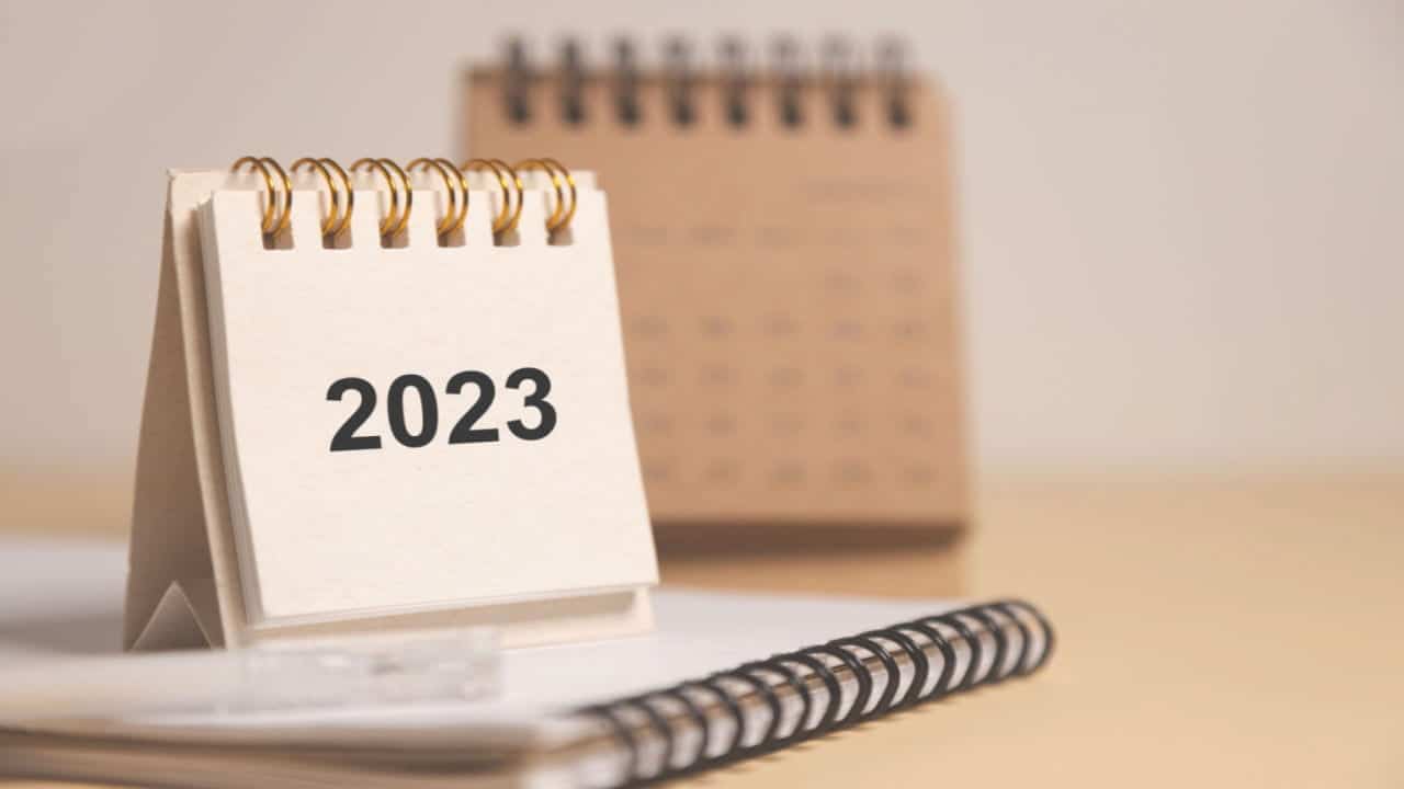 Pequeno calendário de mesa com "2023" escrito, em cima de outro caderno