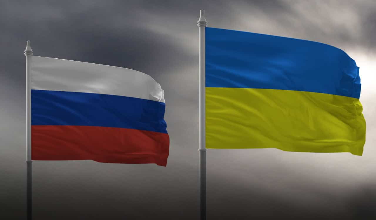 Bandeiras da Rússia e da Ucrânia sob um céu cinzento.