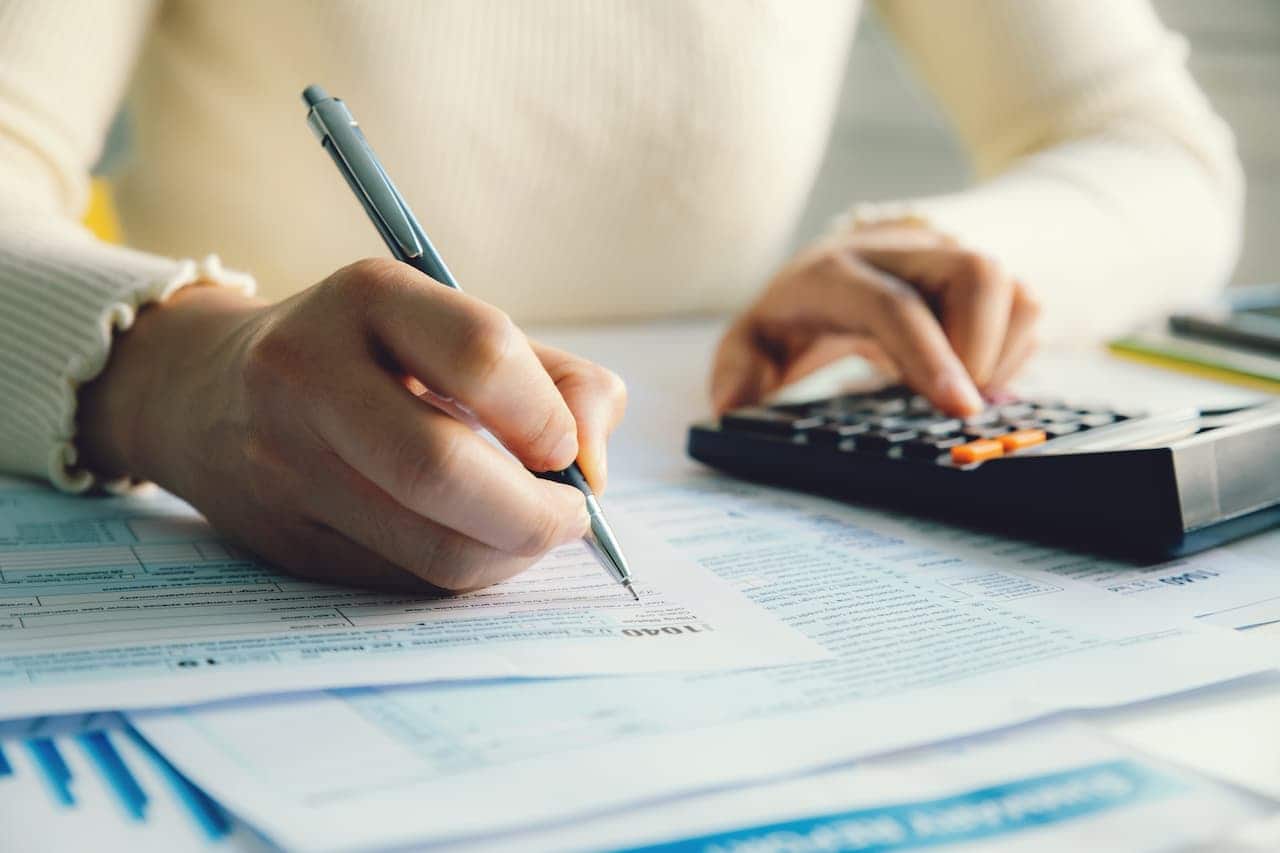 Mãos com uma calculadora e uma caneta, fazendo contas de impostos