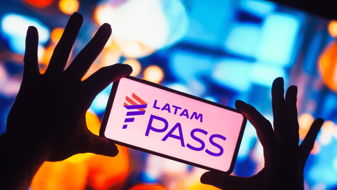 duas mãos segurando um celular. Logotipo do latam pass aparece na tela do no celular