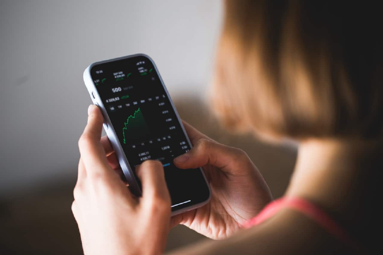 Imagem de uma mulher mexendo em um aplicativo de corretora de investimentos pelo celular.
