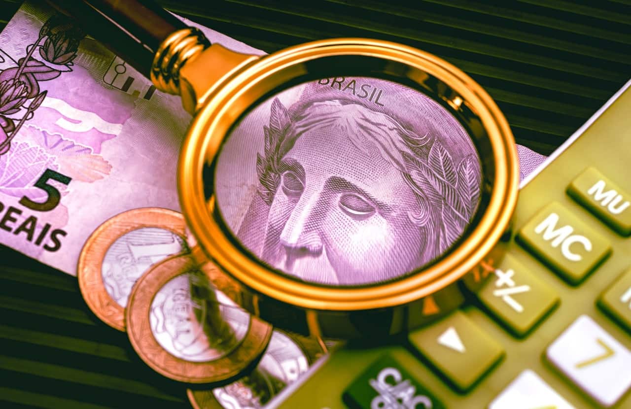 Lupa sobre moedas, calculadora e nota de 5 reais