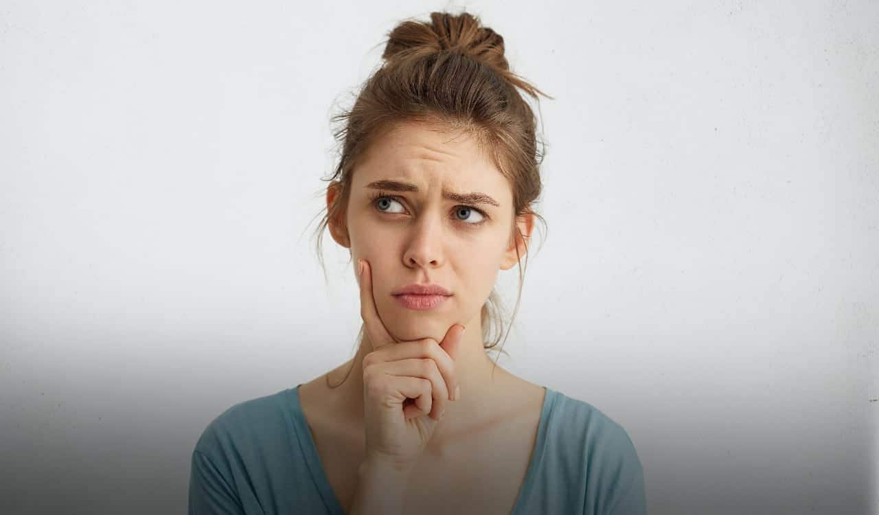 Mulher com a mão no rosto com expressão de dúvida
