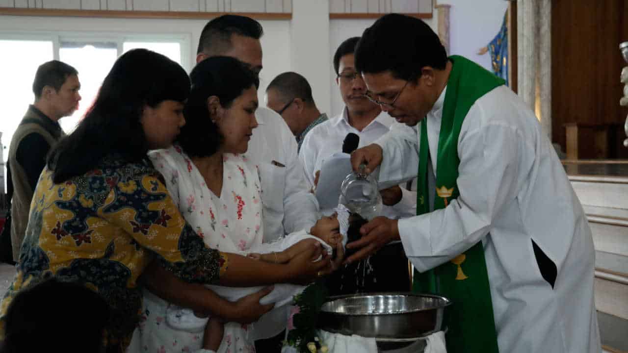 Bebê sendo batizado na igreja católica com os padrinhos o segurando no colo