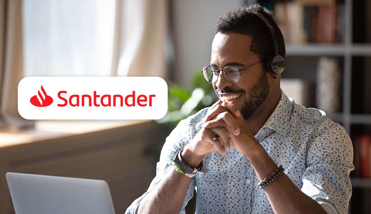 Um homem negro, com as mãos abaixo do queixo, olhando, sorridente, para a tela do notebook. Ao lado, a logo do banco Santander.