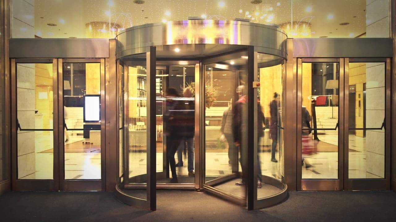 Porta giratória na entrada de um edifício com algumas pessoas passando dentro.
