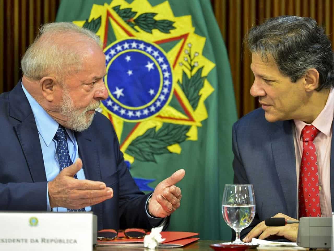 Imagem de Lula e Haddad conversando sentados a uma mesa.