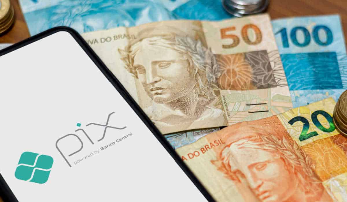 aparelho celular com o símbolo do pix sobre uma tela branca, o aparelho está sobre cédulas de 20, 50 e 100 reais