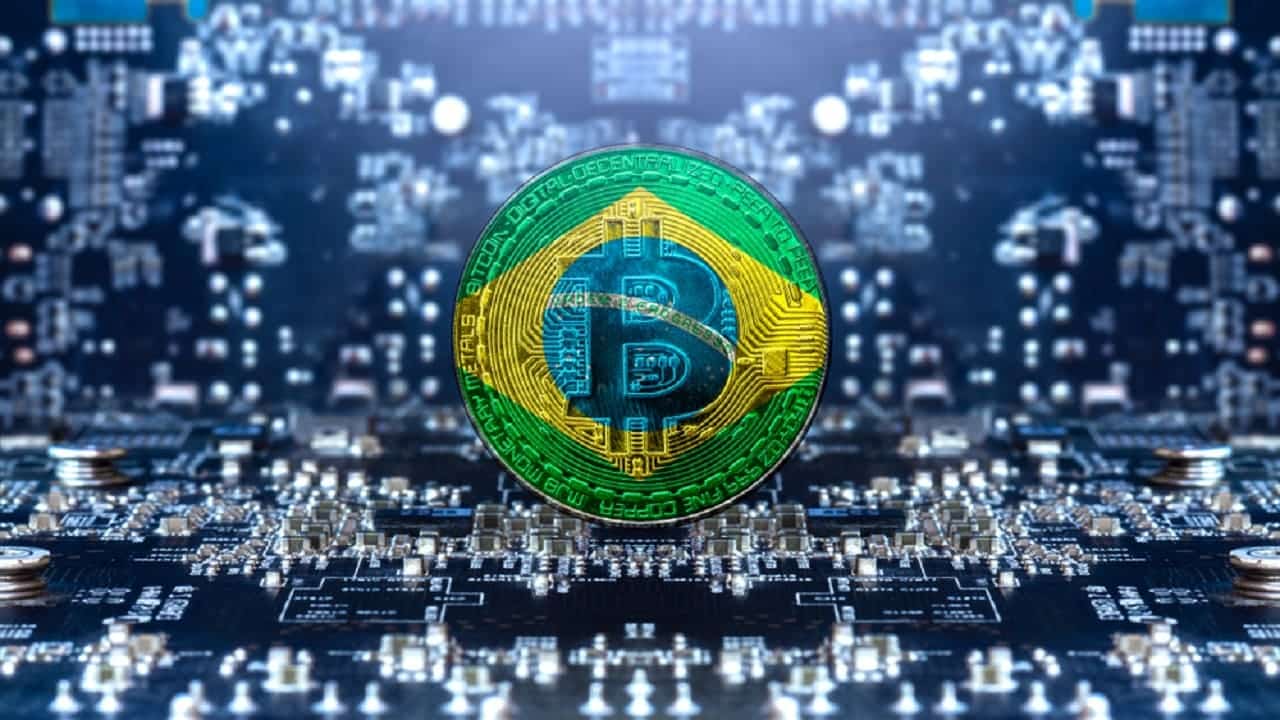 Imagem de uma moeda digital estampada com a bandeira do Brasil. Ao fundo, um circuito de computador.