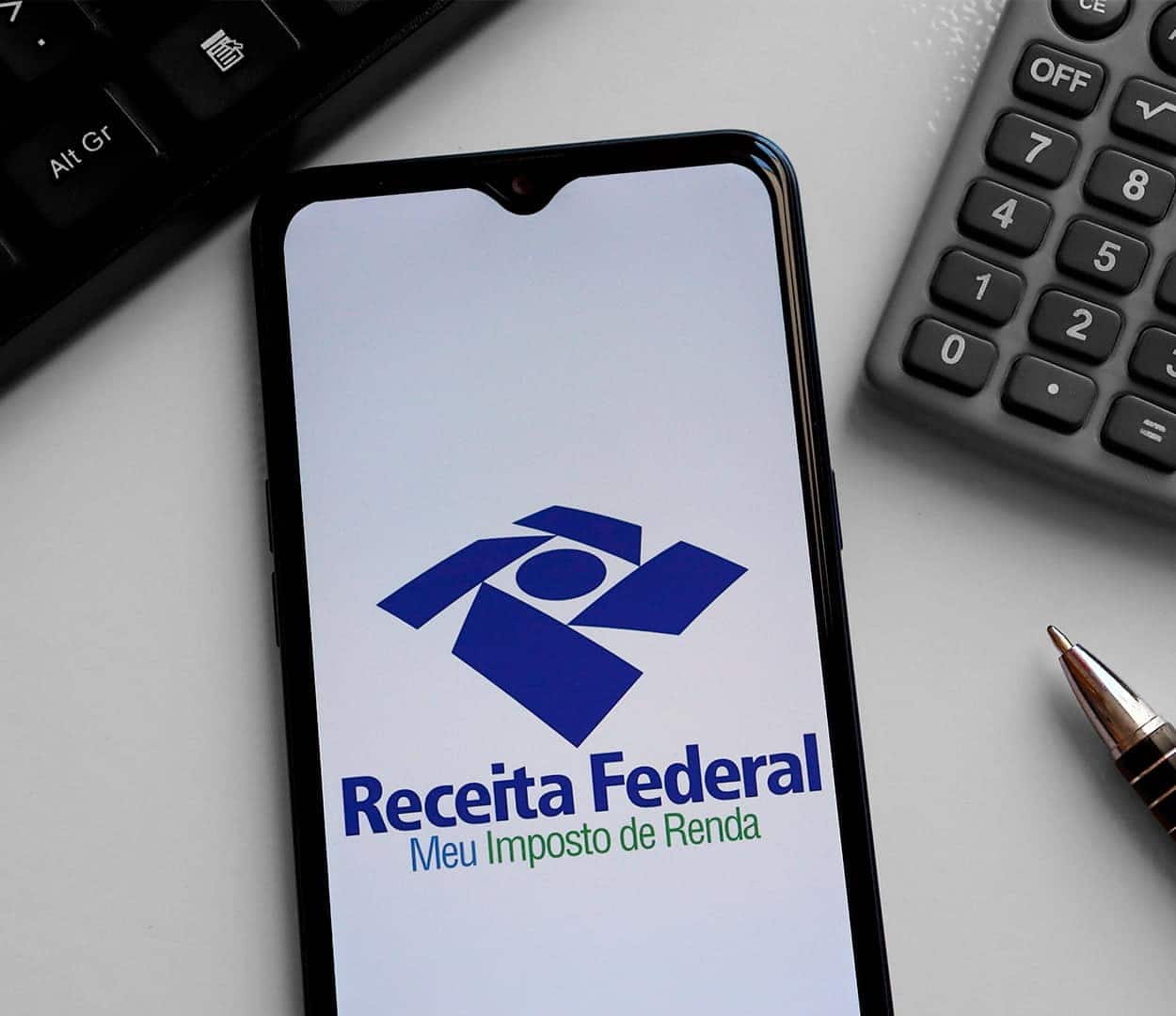 Celular com aplicativo da Receita Federal e Imposto de Renda aberto em cima de uma mesa branca