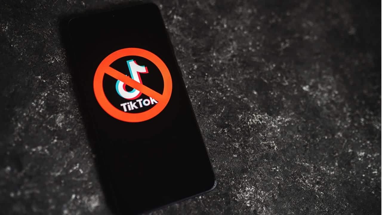 Celular sobre uma mesa mostrando o logo do aplicativo TikTok com um símbolo de proibição na tela.