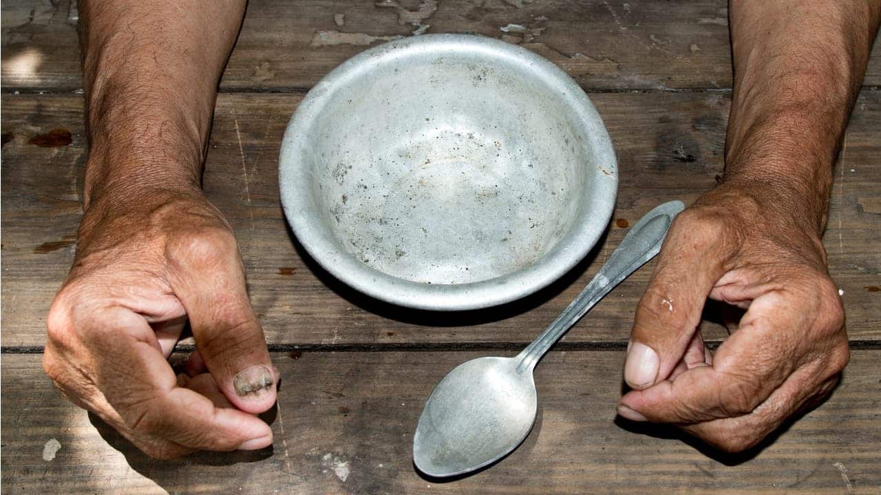 imagem de mãos machucadas de trabalhador com um prato vazio e uma colher em cima da mesa, fazendo alusão à fome e escravidão