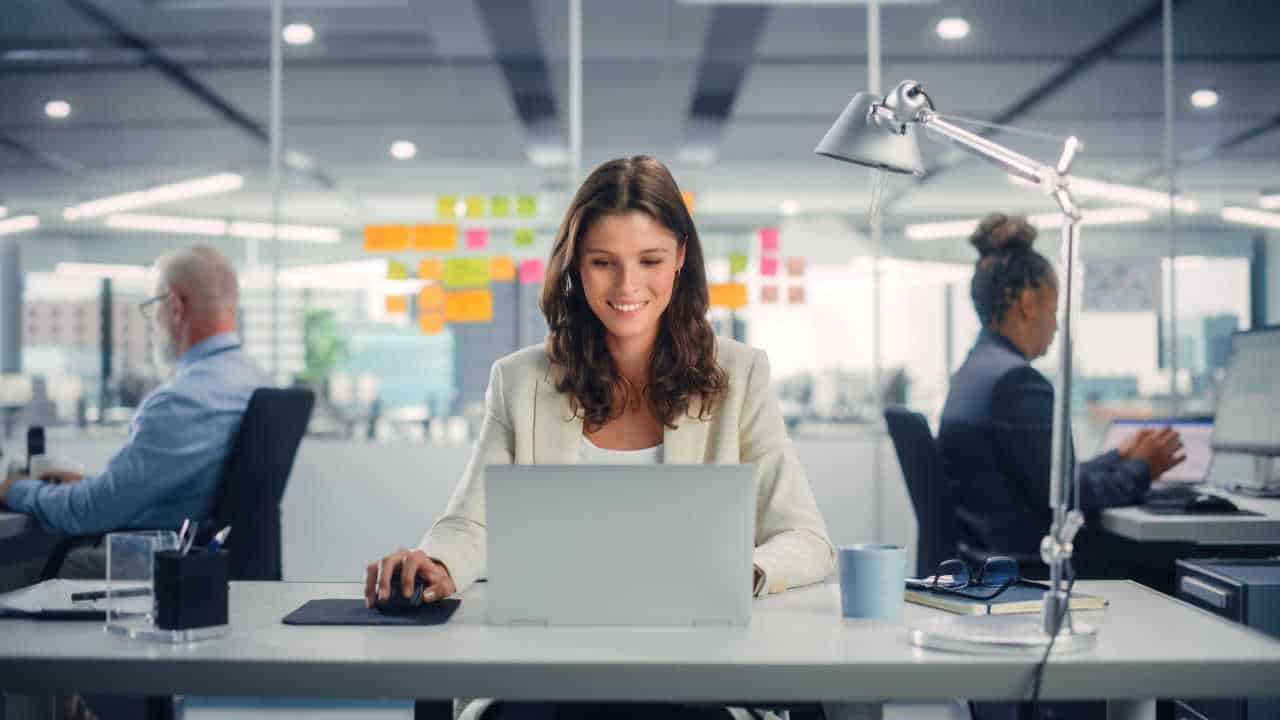 Mulher em frente a um computador no escritório com os colegas da empresa