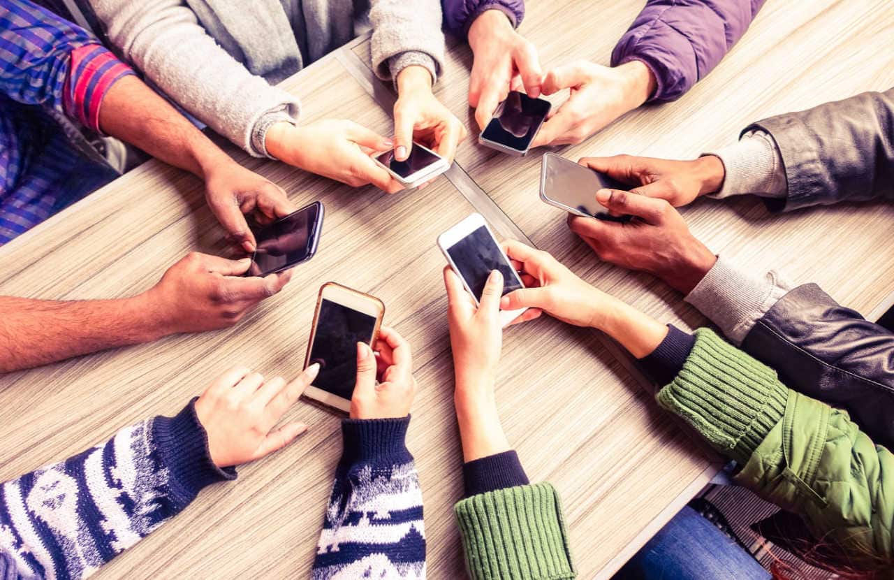 Várias mãos segurando celulares sobre uma mesa