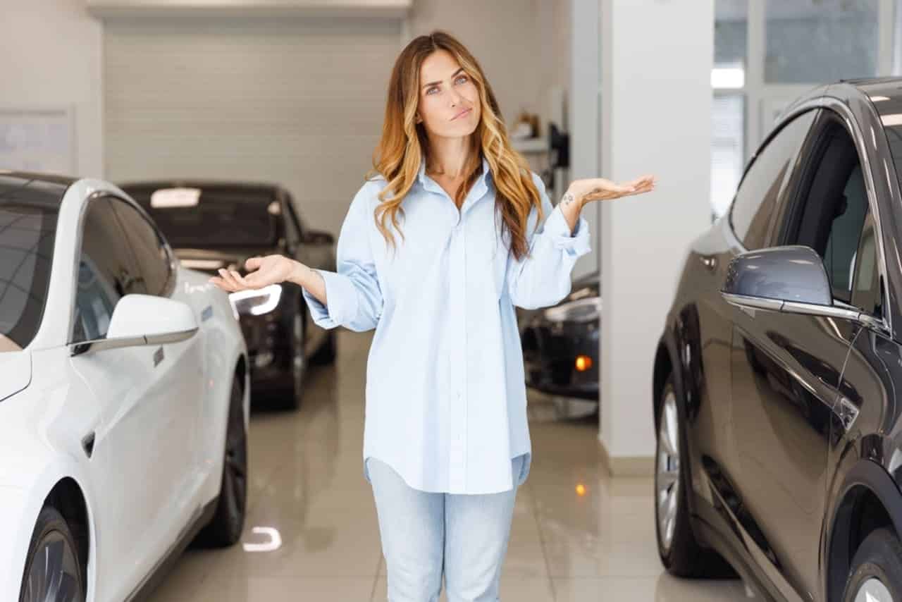Mulher parada entre doi carros com as mãos levantadas expressando dúvida