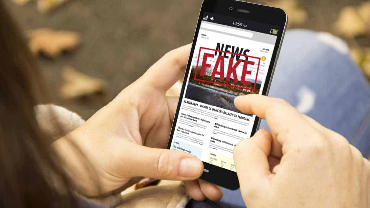Pessoa mexendo em celular com o escrito "Fake News" na tela inicial