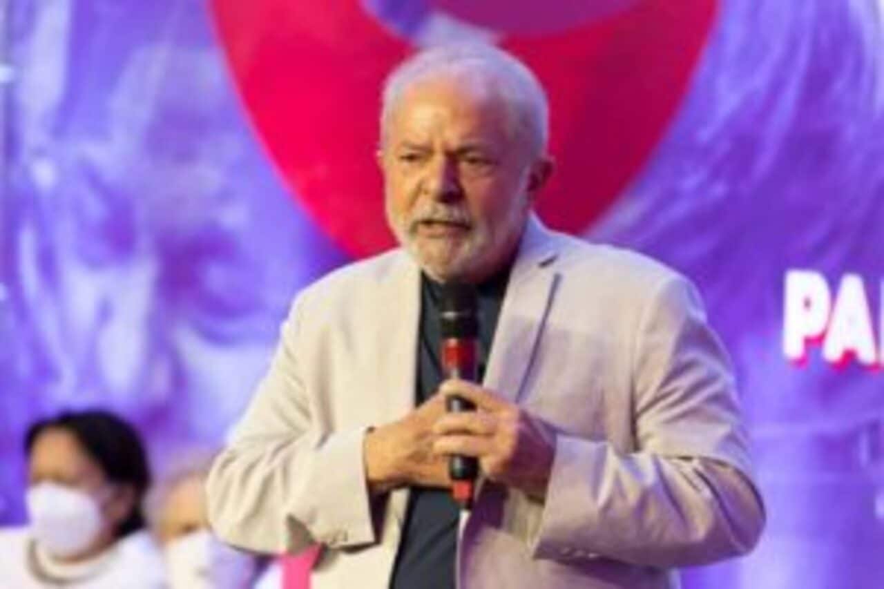 Presidente Lula em discurso com microfone na mão. Fundo roxo e vermelho