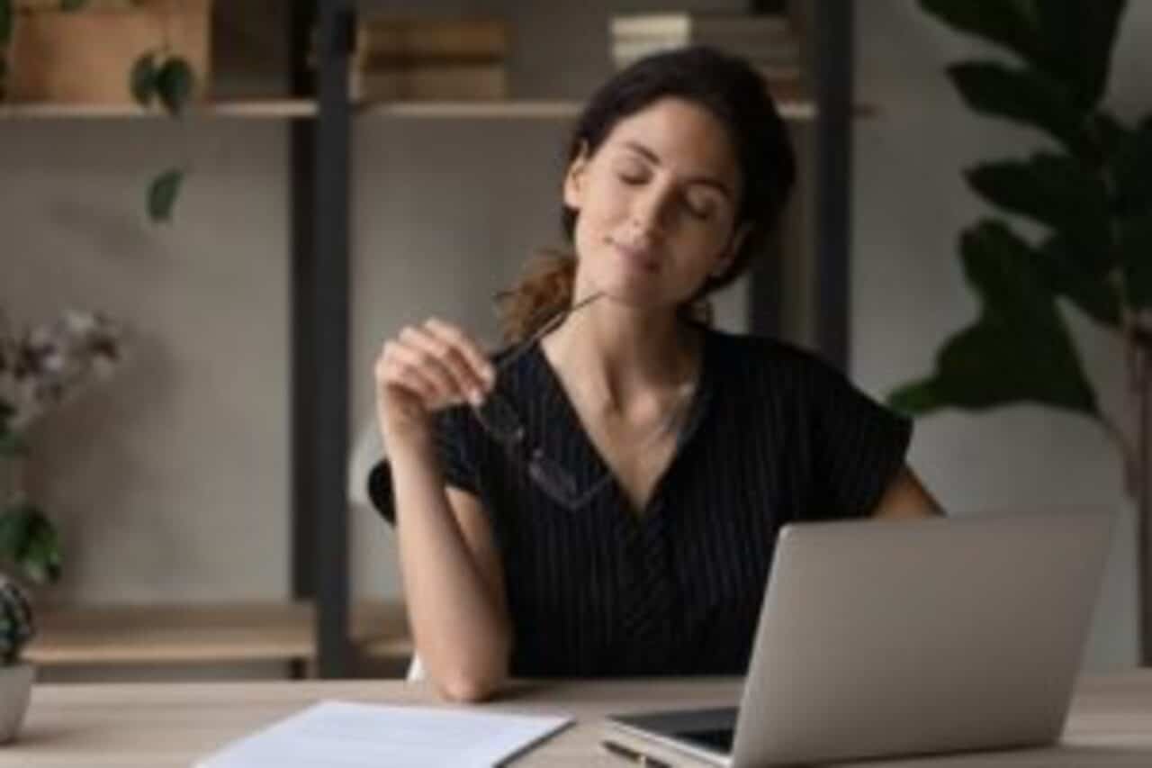 Mulher em frente a notebook com os olhos fechados e semblante de alívio