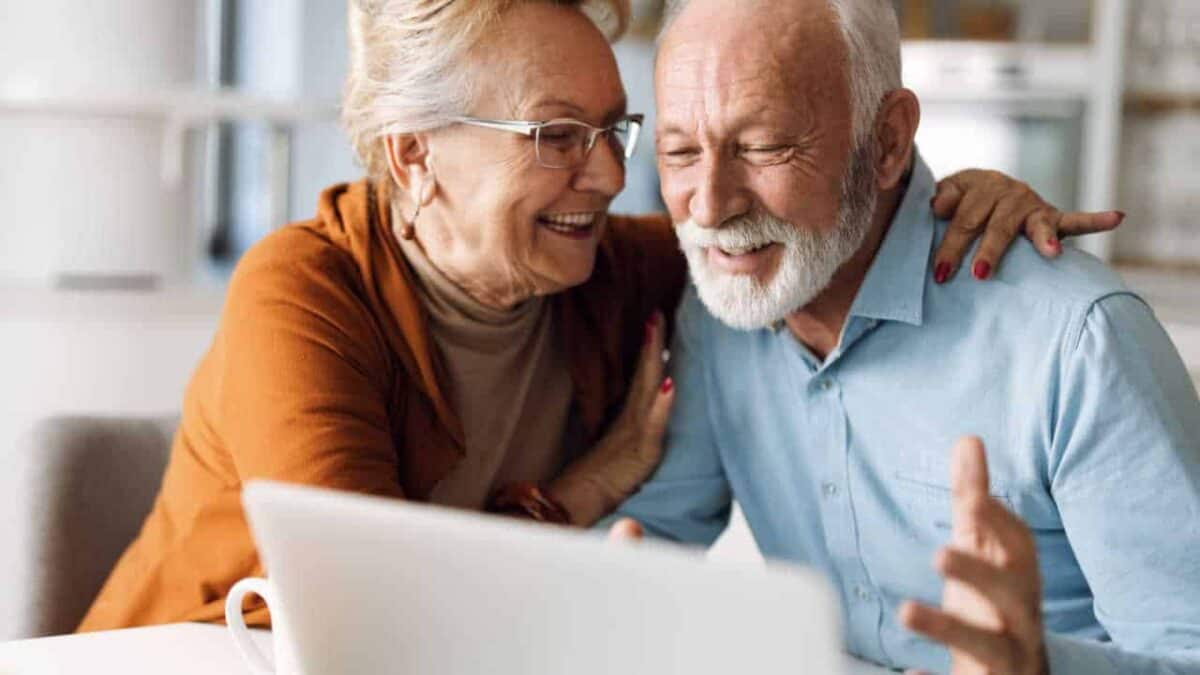 Casal de idosos felizes e sorrindo, olhando para a tela do computador