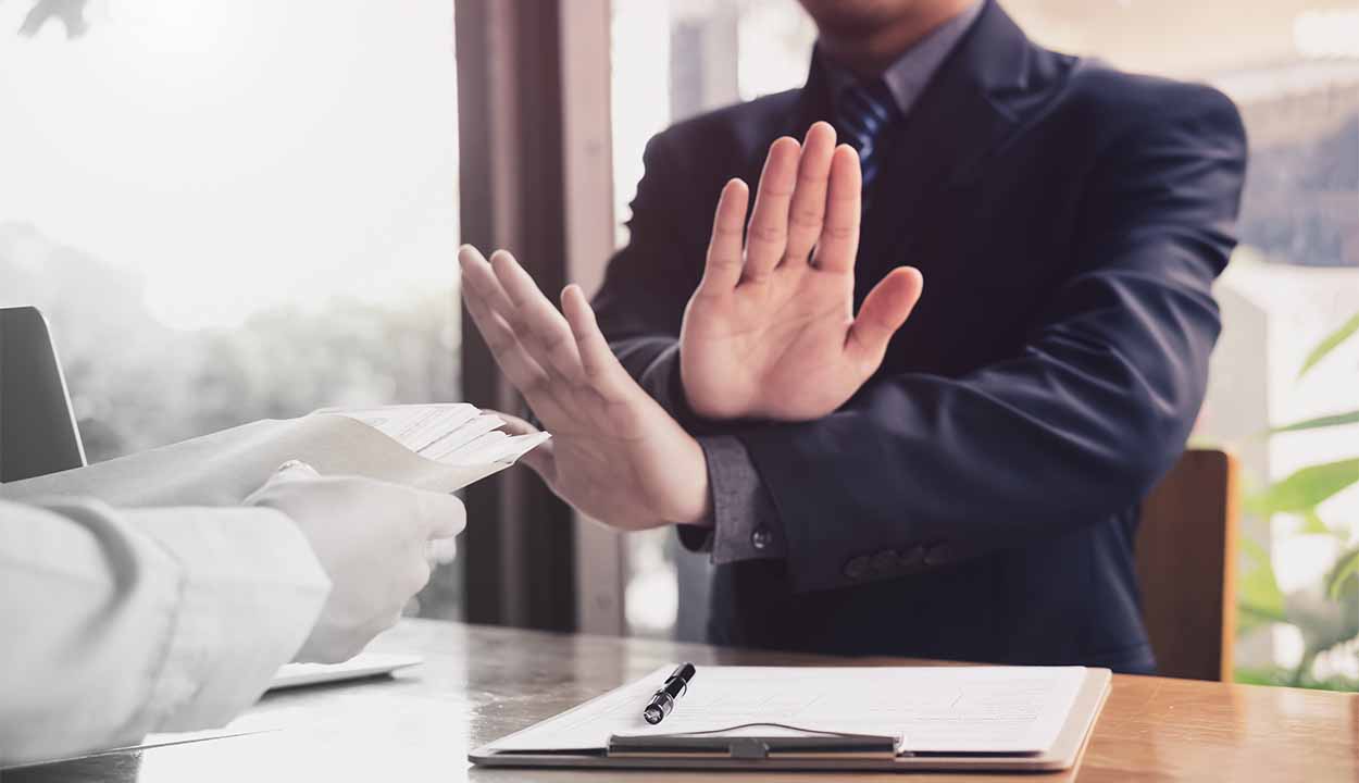Mãos de uma pessoa simbolizando uma recusa diante de outra pessoa entregando papéis