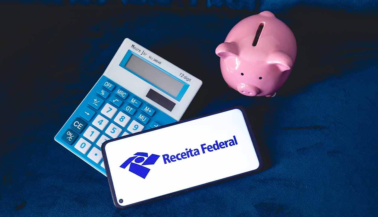 Celular que mostra logo da Receita Federal ao lado de uma calculadora e de um cofrinho em formato de porco