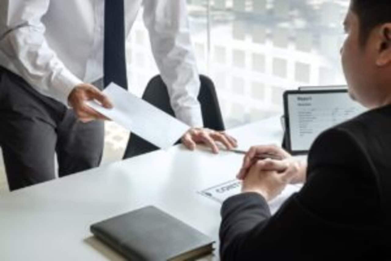 trabalhador de terno entregando carta de demissão por justa causa para empregador sentado em uma mesa de escritório