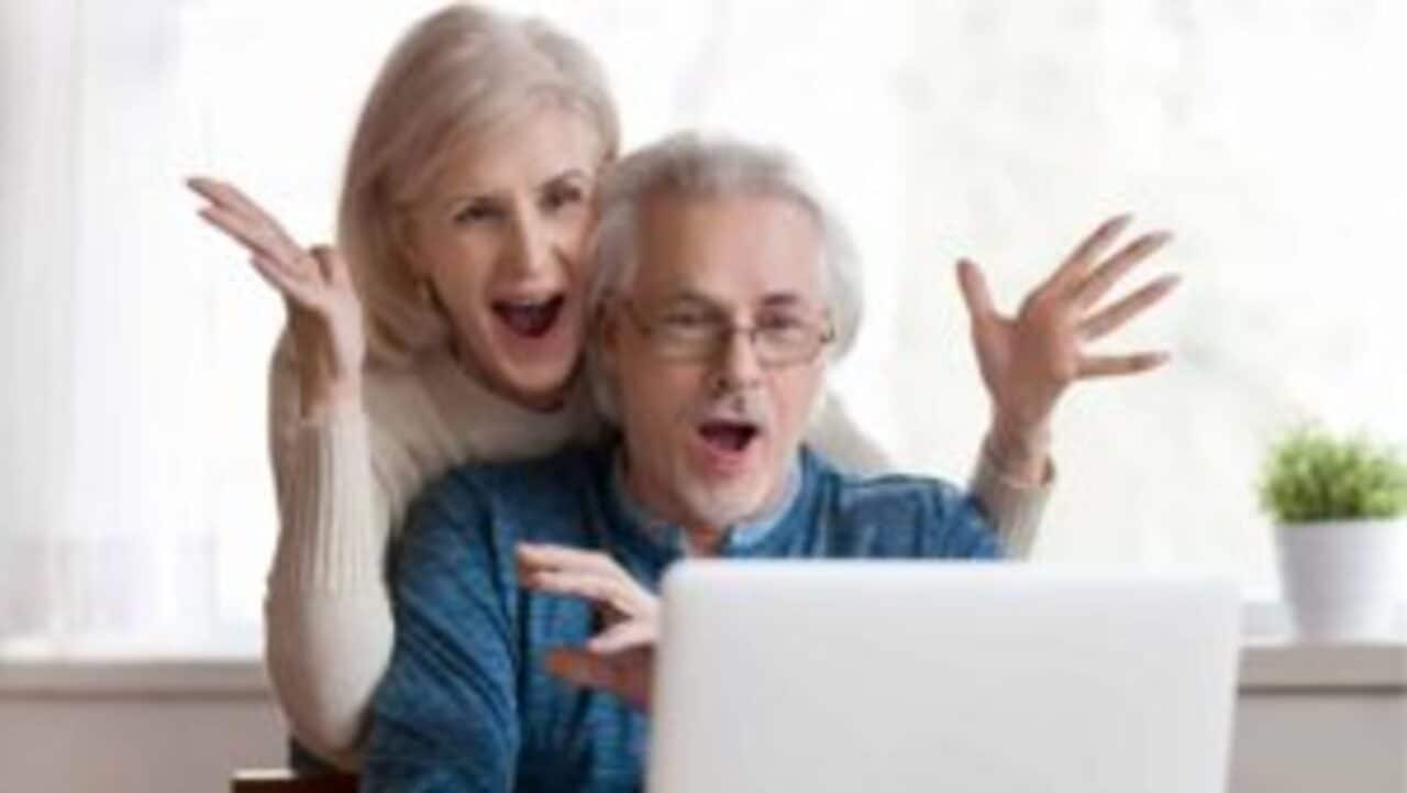 Casal de aposentados comemorando em frente ao notebook