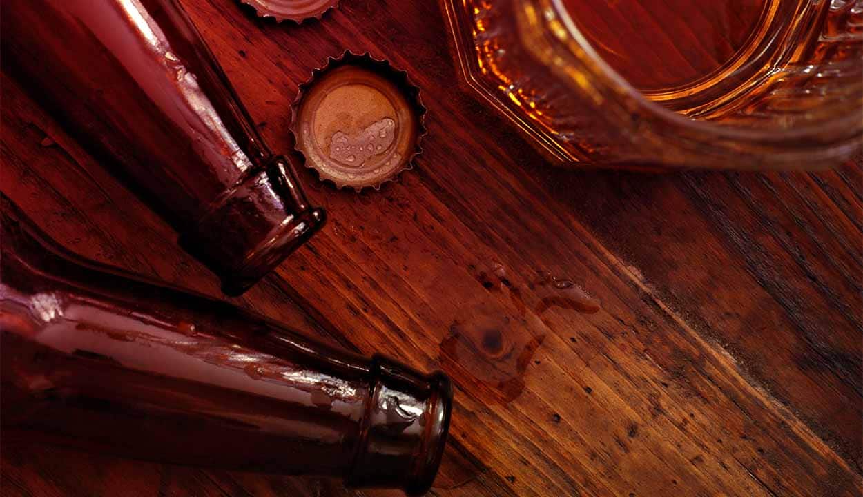 Closeup na imagem de garrafas de cerveja caidas em uma mesa, tampas e um copo