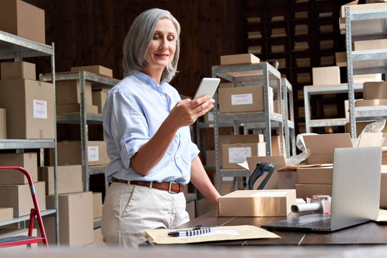 Mulher comerciante segurando celular atrás de balcão de atendimento