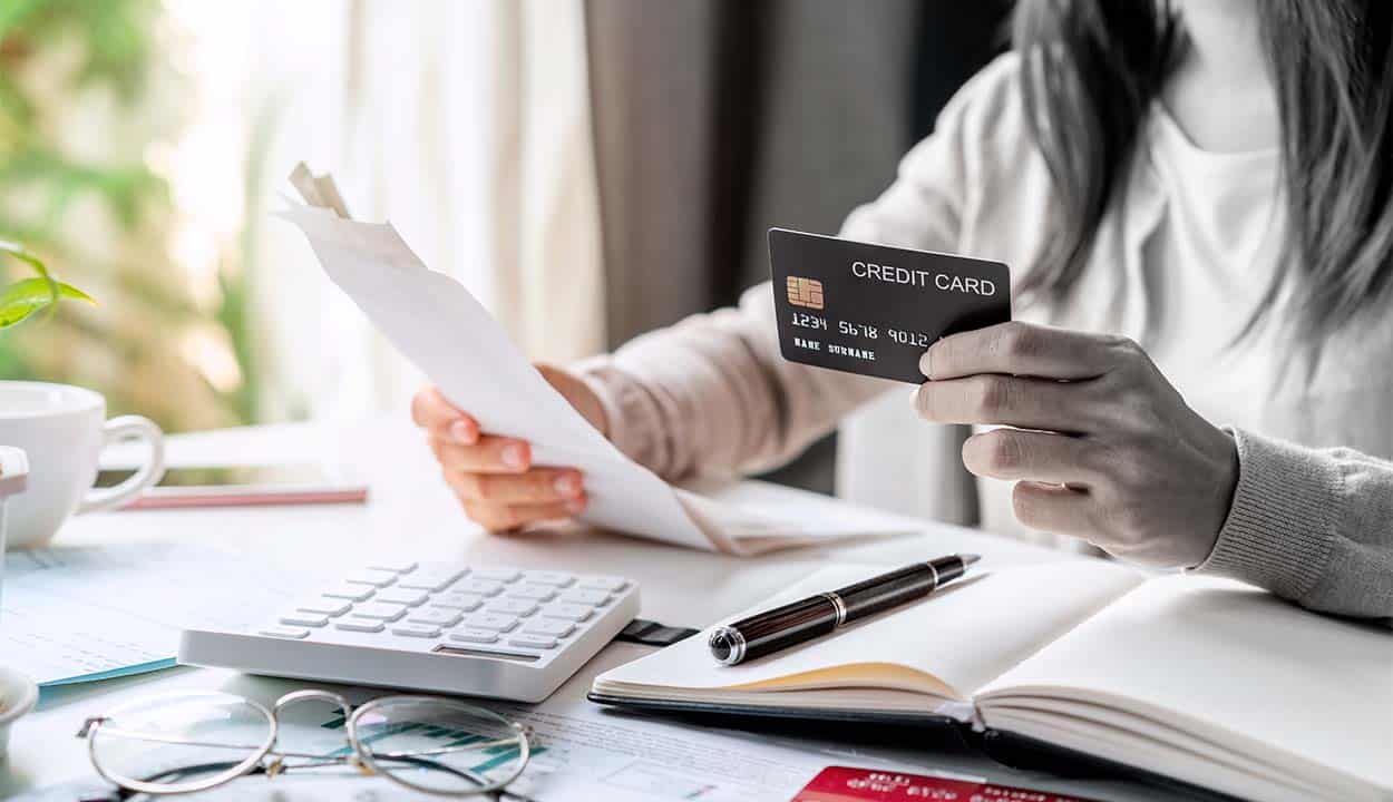 Mão segurando cartão de crédito e papeis